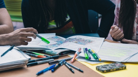 Picture of three diverse individuals collaborating on a project. Pens spewed all over the table,