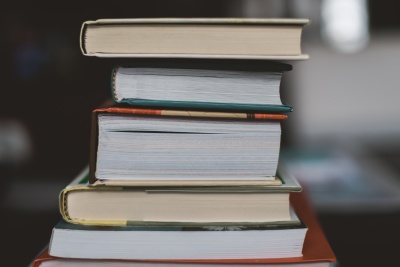 A stack of hardcover books rests on a table, the spines facing to the left.